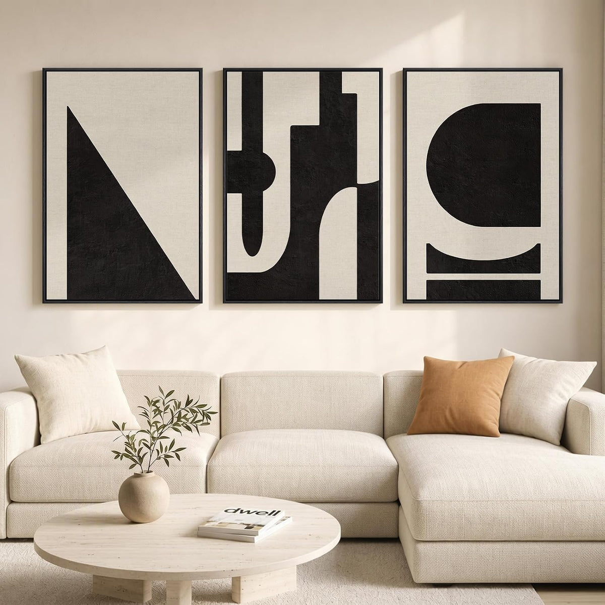 Three framed minimalist prints with large black geometric shapes on a beige background above a cream sofa and round wood