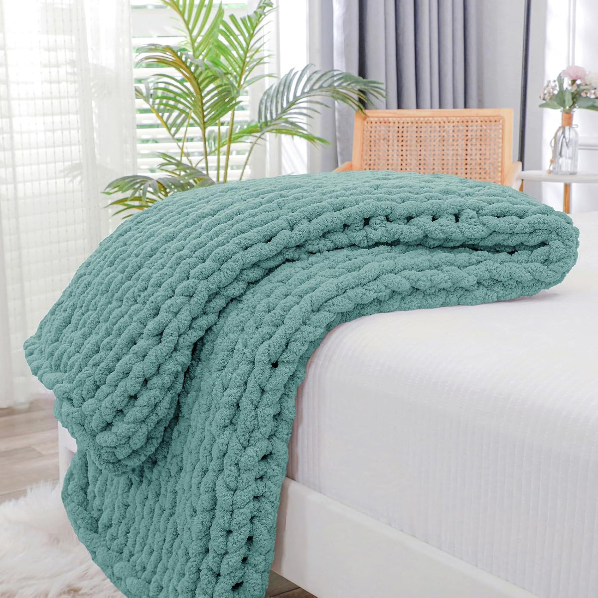 Teal-green chunky throw folded and draped over the corner of a white mattress.