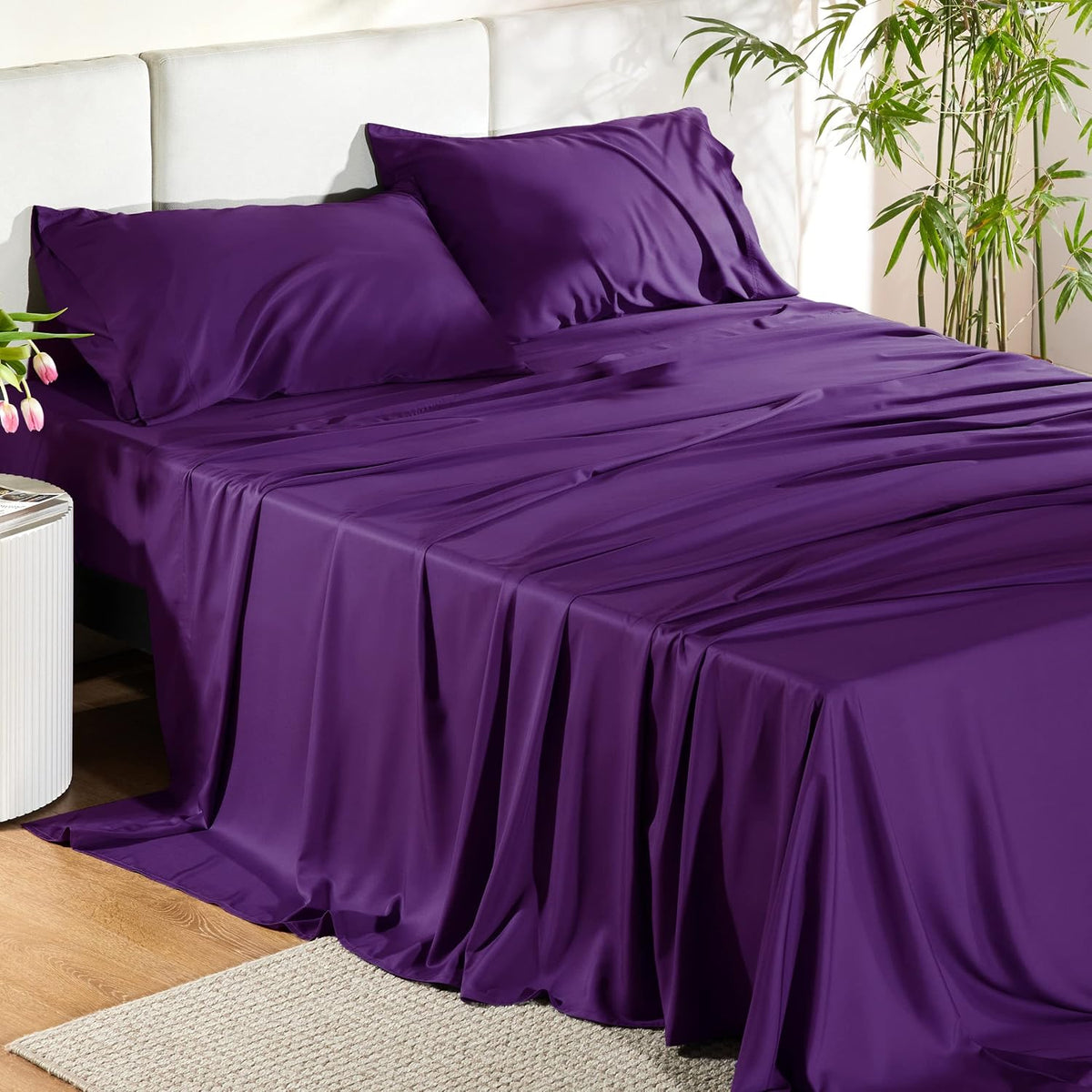 Wide shot of a bed made with vivid purple sheets and two pillows, fabric flowing to the floor