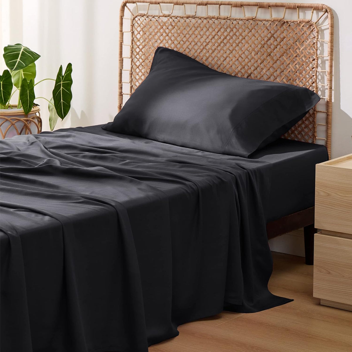 Side view of a bed with dark charcoal sheets draped over the mattress and one pillow