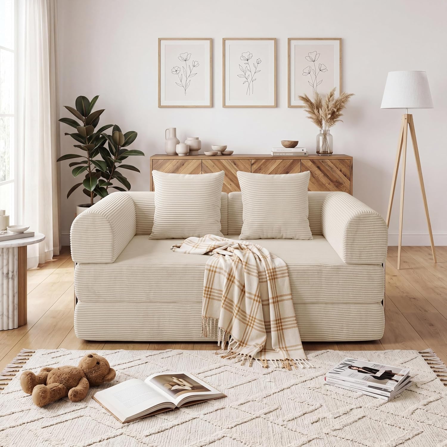 Cream corduroy sofa with two matching pillows and a plaid throw centered in a neutral, sunlit room