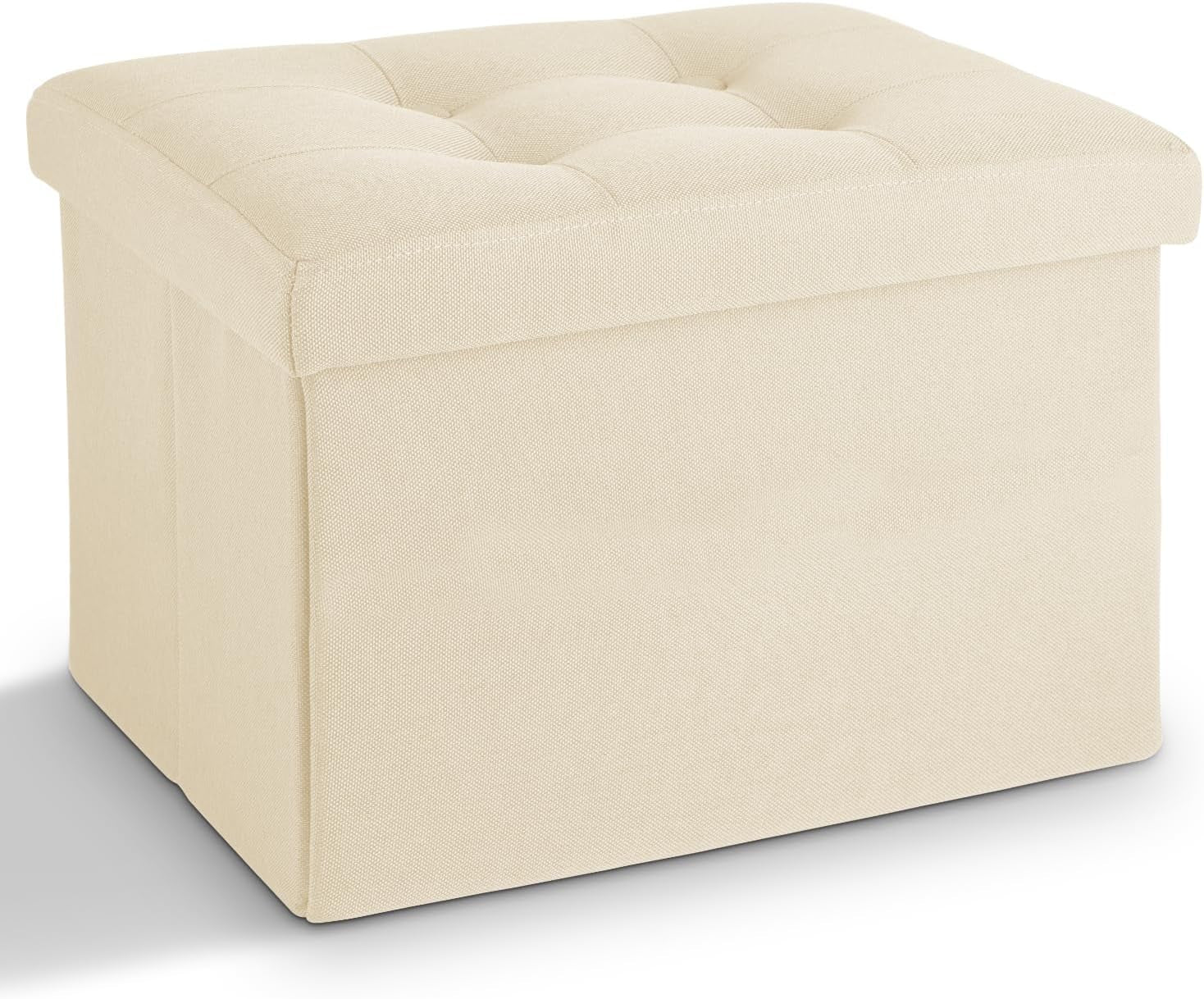 Three-quarter view of a square cream fabric storage ottoman with tufted cushioned top.