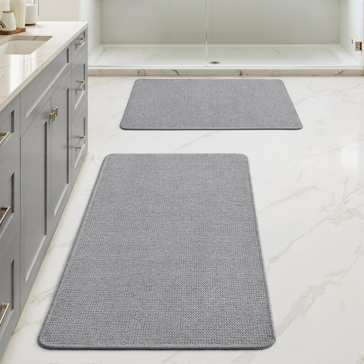 Light gray rectangular bath mat and matching smaller mat placed in front of a walk-in shower