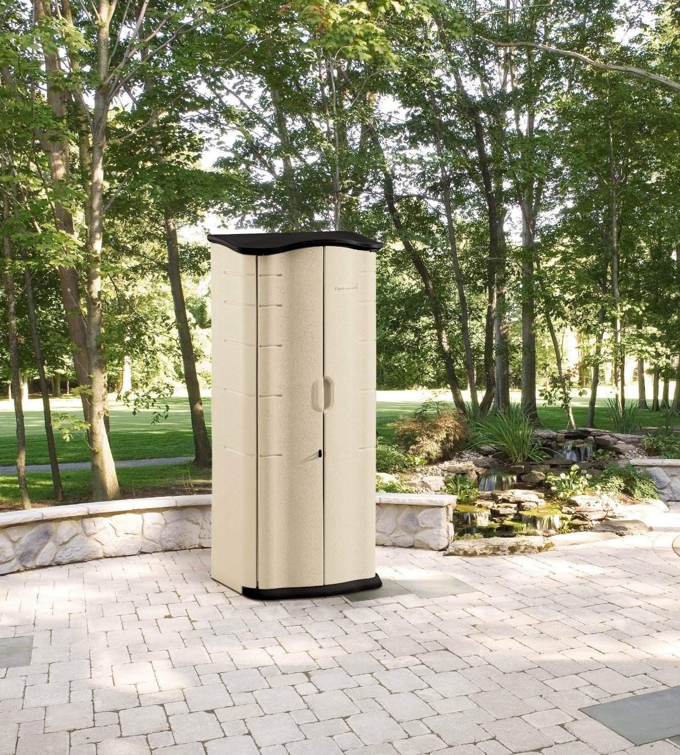Beige resin storage shed on a stone patio with trees and landscaping in the background