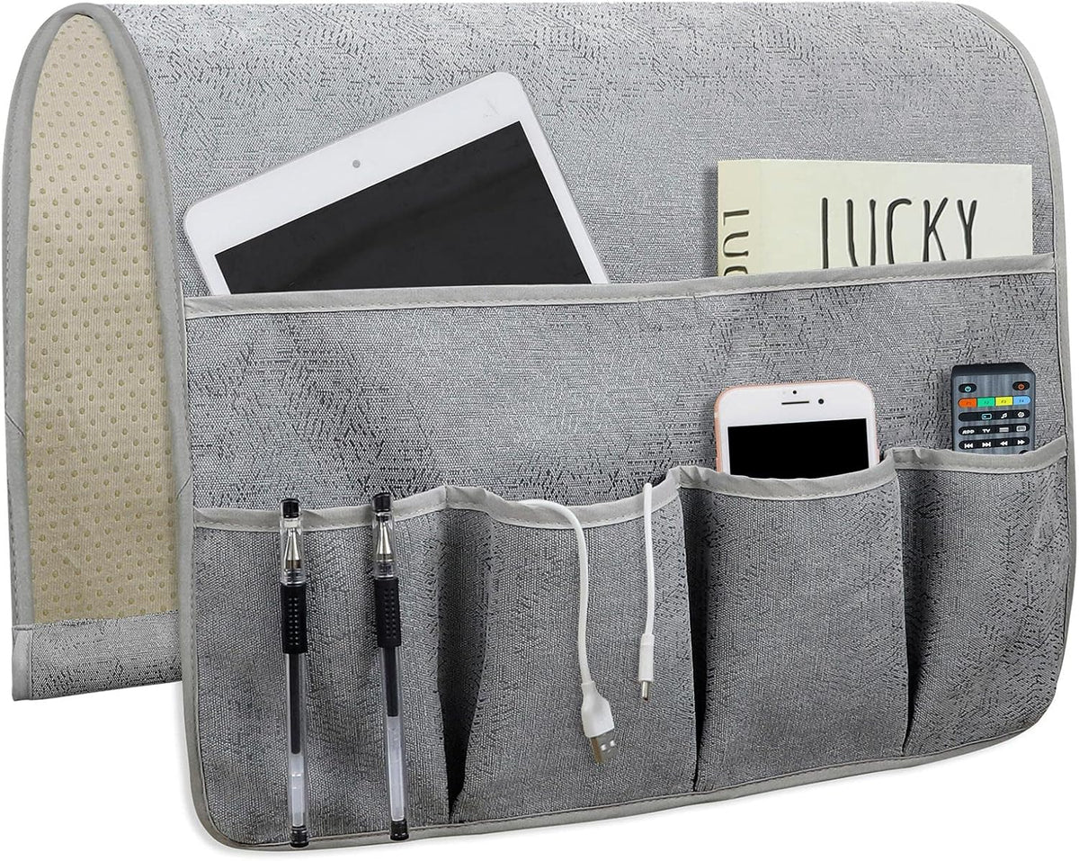 Light gray linen organizer front with five pockets holding tablet, pens, cables and remote; non-slip underside visible.