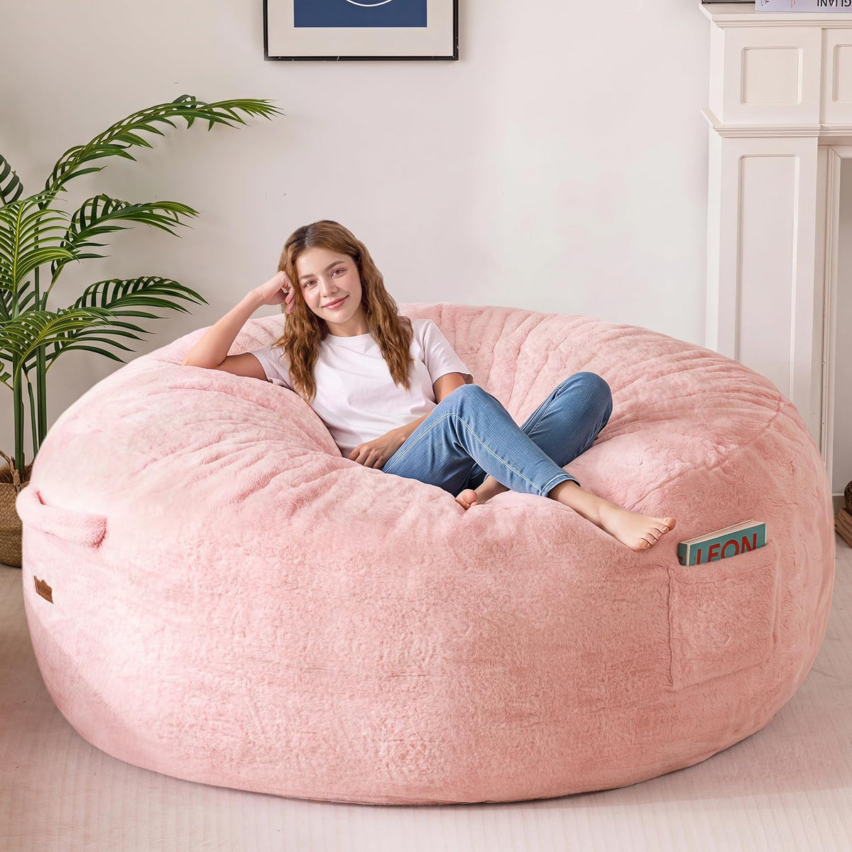 Angled view of a woman lounging on a large blush pink bean bag with a book tucked in the pocket.