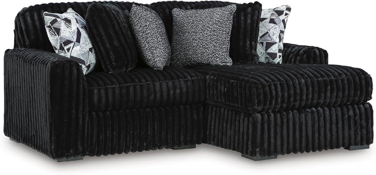 Black jumbo-corduroy chaise sectional shown from a low side angle with decorative pillows