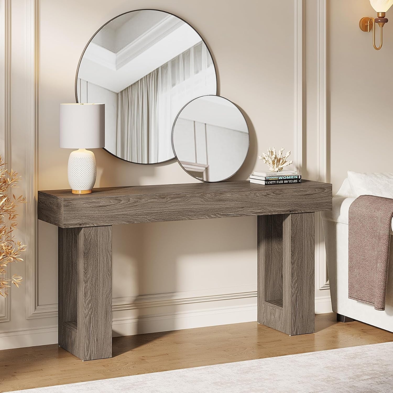 Side-angle view of grey console topped with two round mirrors and a table lamp, sofa arm visible at right.