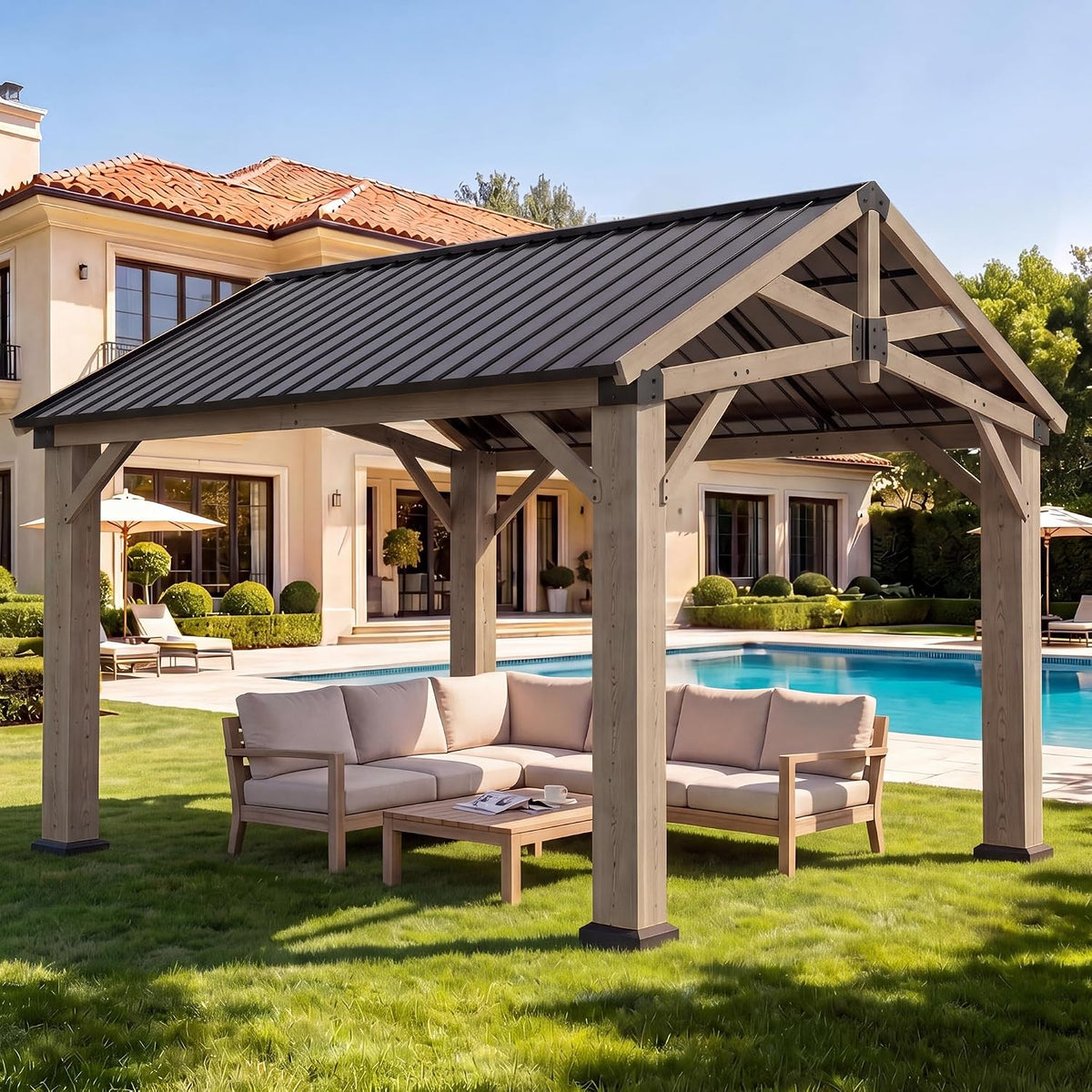 Daytime poolside setting with the wooden gazebo placed on a grassy lawn and a sectional sofa beneath it.