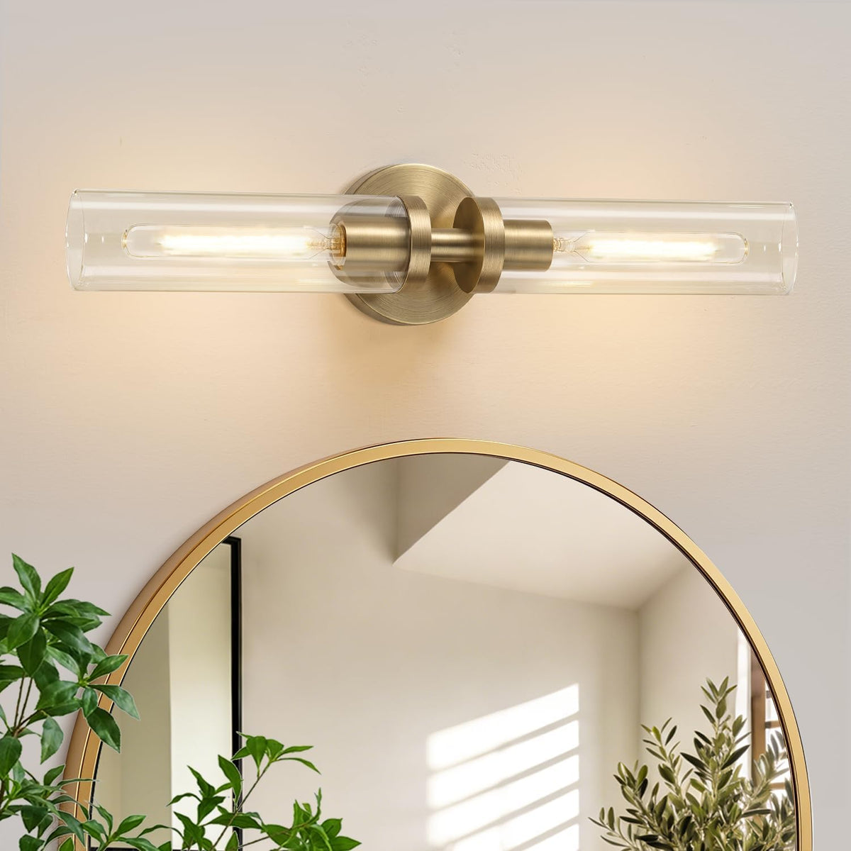 Single horizontal brushed-gold double-tube sconce mounted above a round mirror in a softly lit bathroom setting.