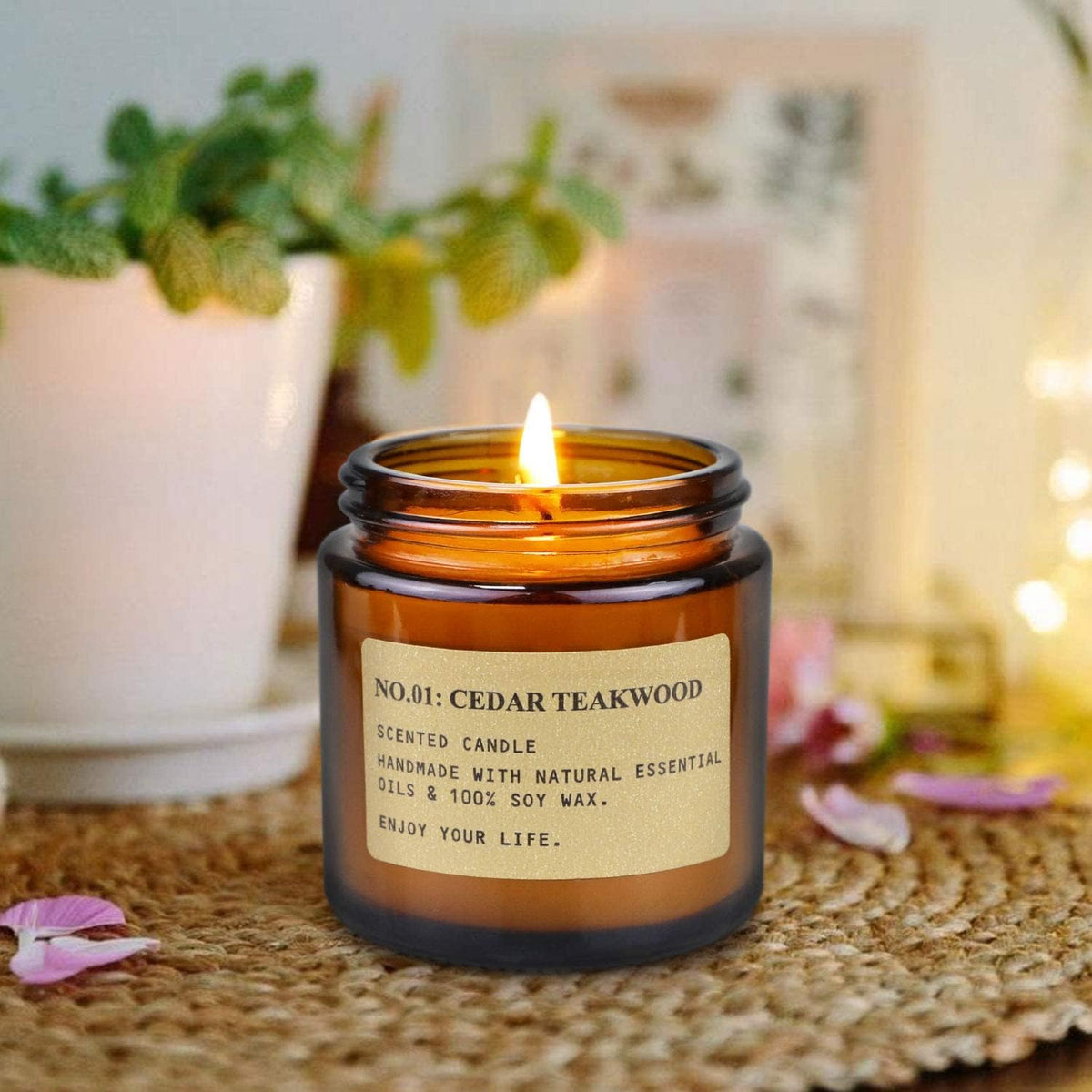 Close-up of a lit amber glass jar candle labeled 'Cedar Teakwood' on a wooden board