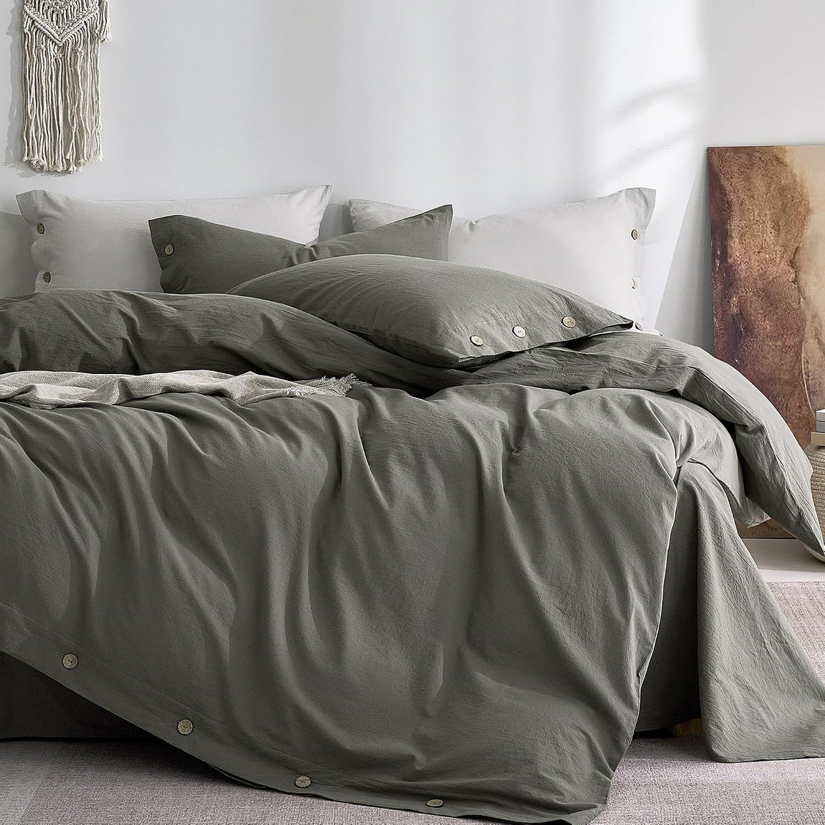 Low-angle view of a bed with dark charcoal linen-like duvet and buttoned pillow shams against a white wall