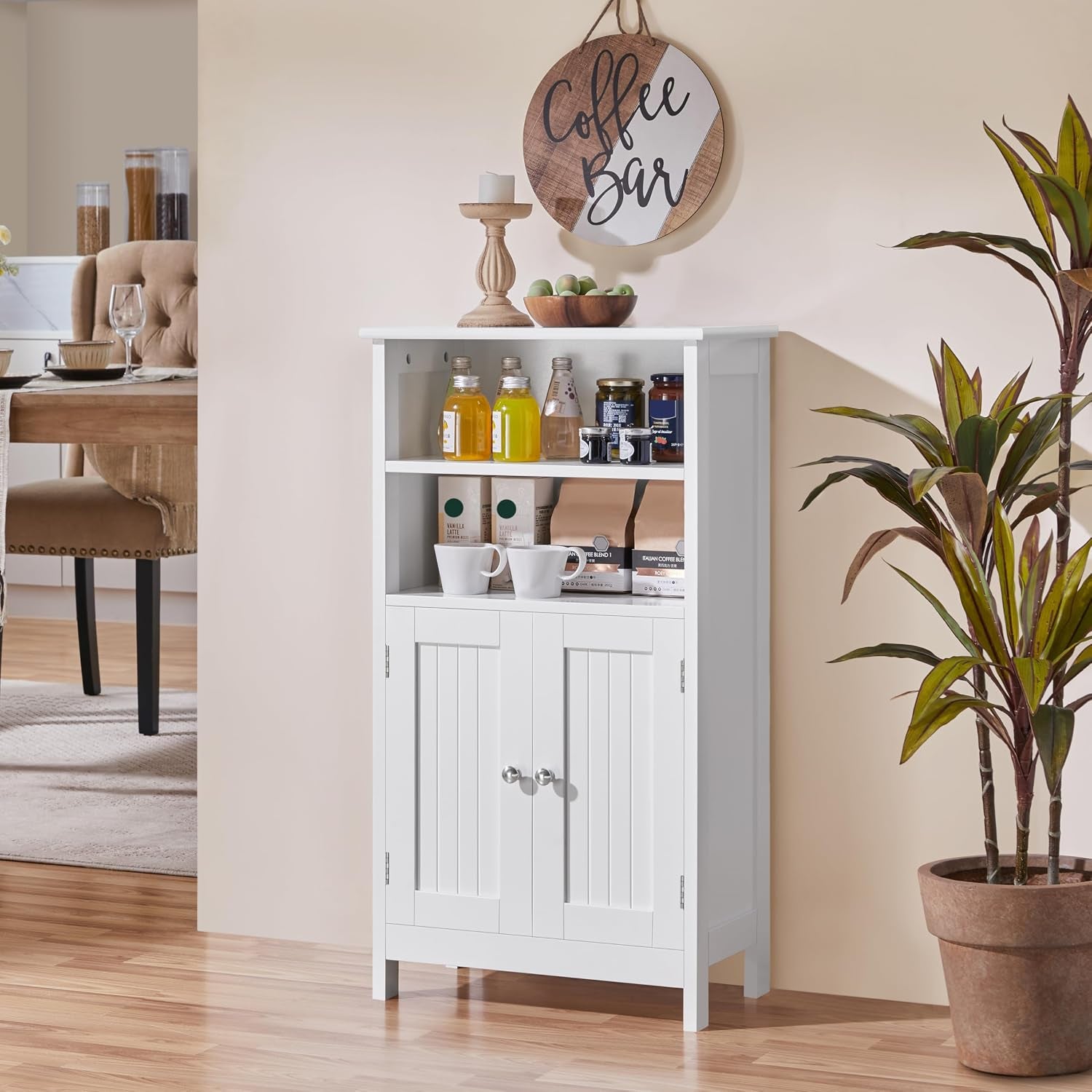 Front-facing white storage cabinet staged with jars, cups and coffee items on the open shelves and a potted plant to the