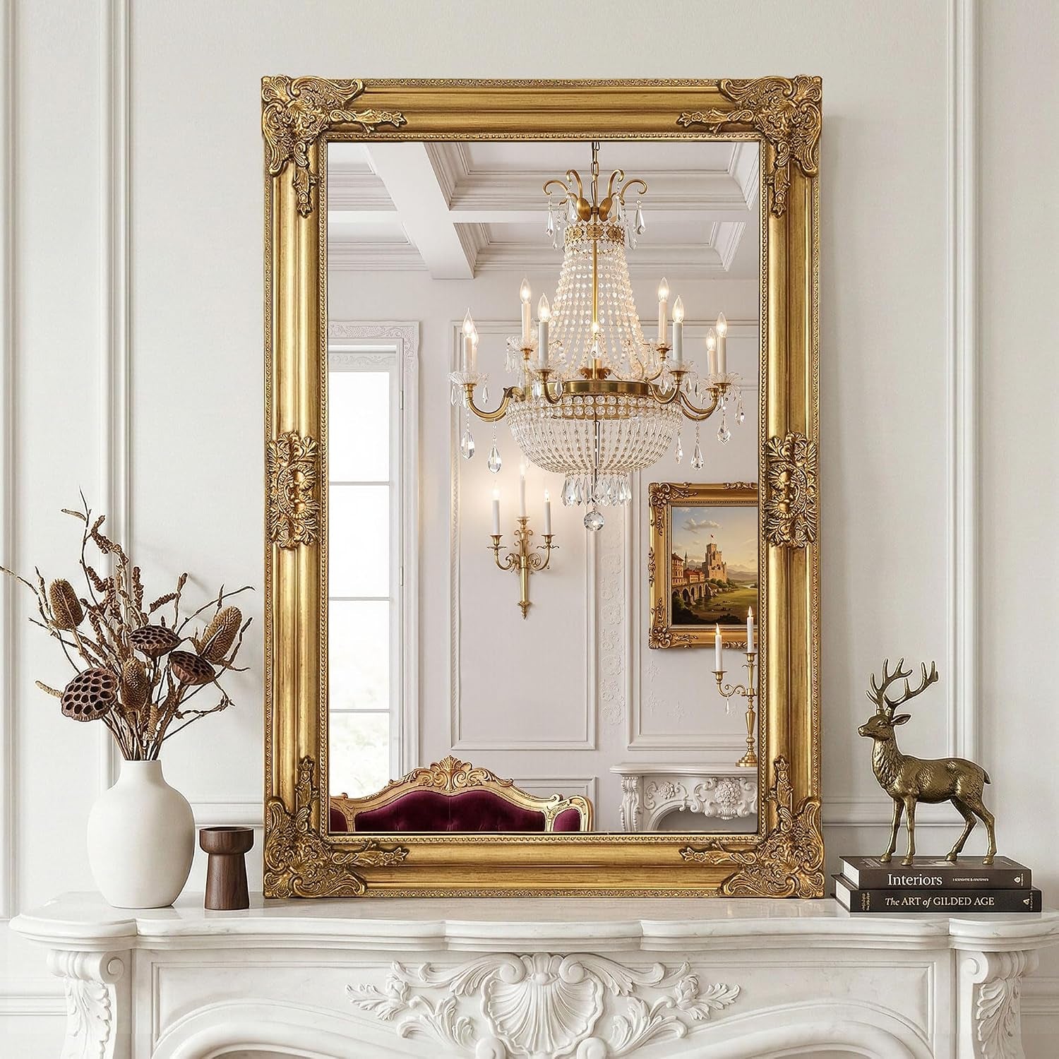 Ornate antique gold framed mirror leaning on a white carved mantel reflecting a chandelier and wall art.