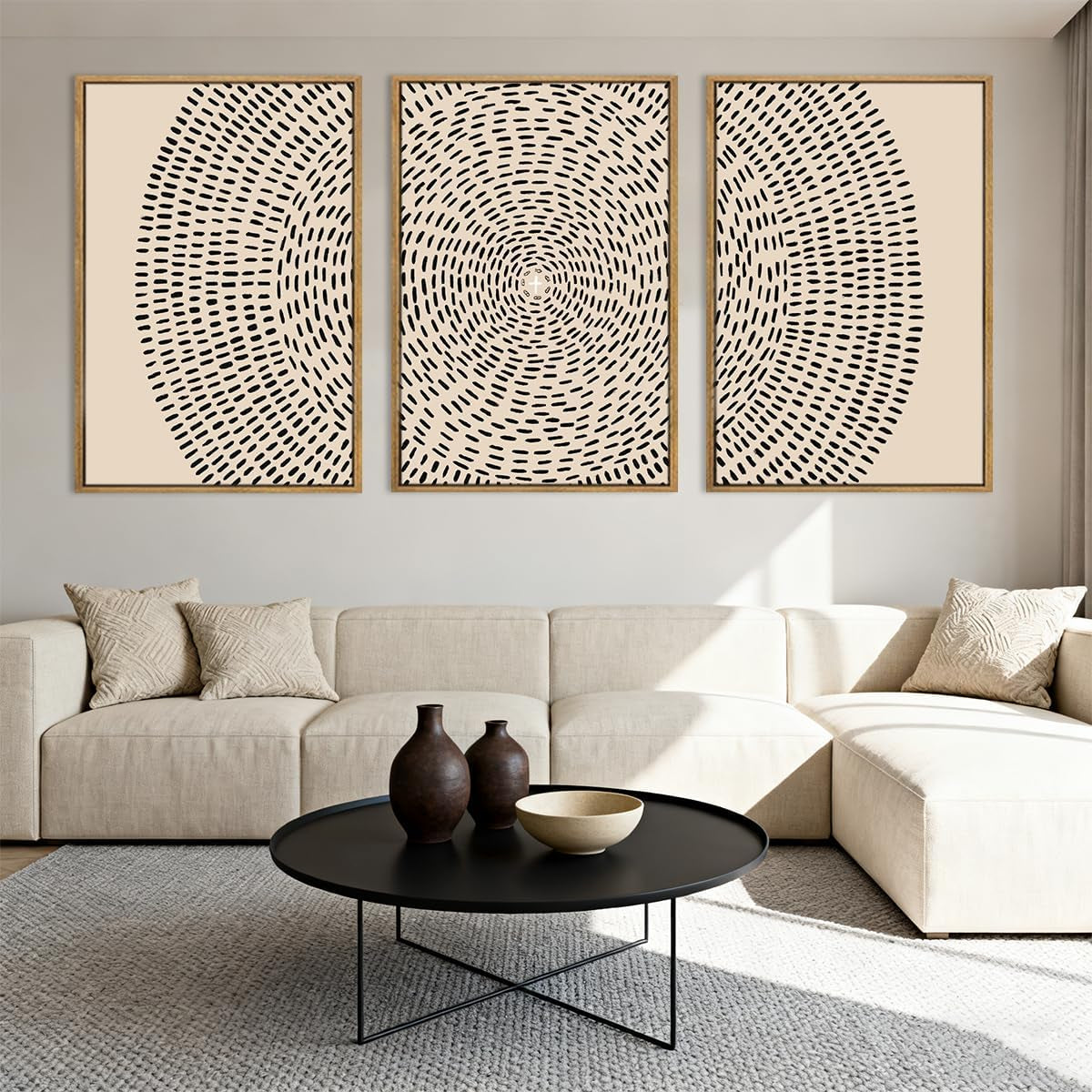 Three framed beige and black canvas panels with circular dash pattern arranged above a sectional sofa and round table
