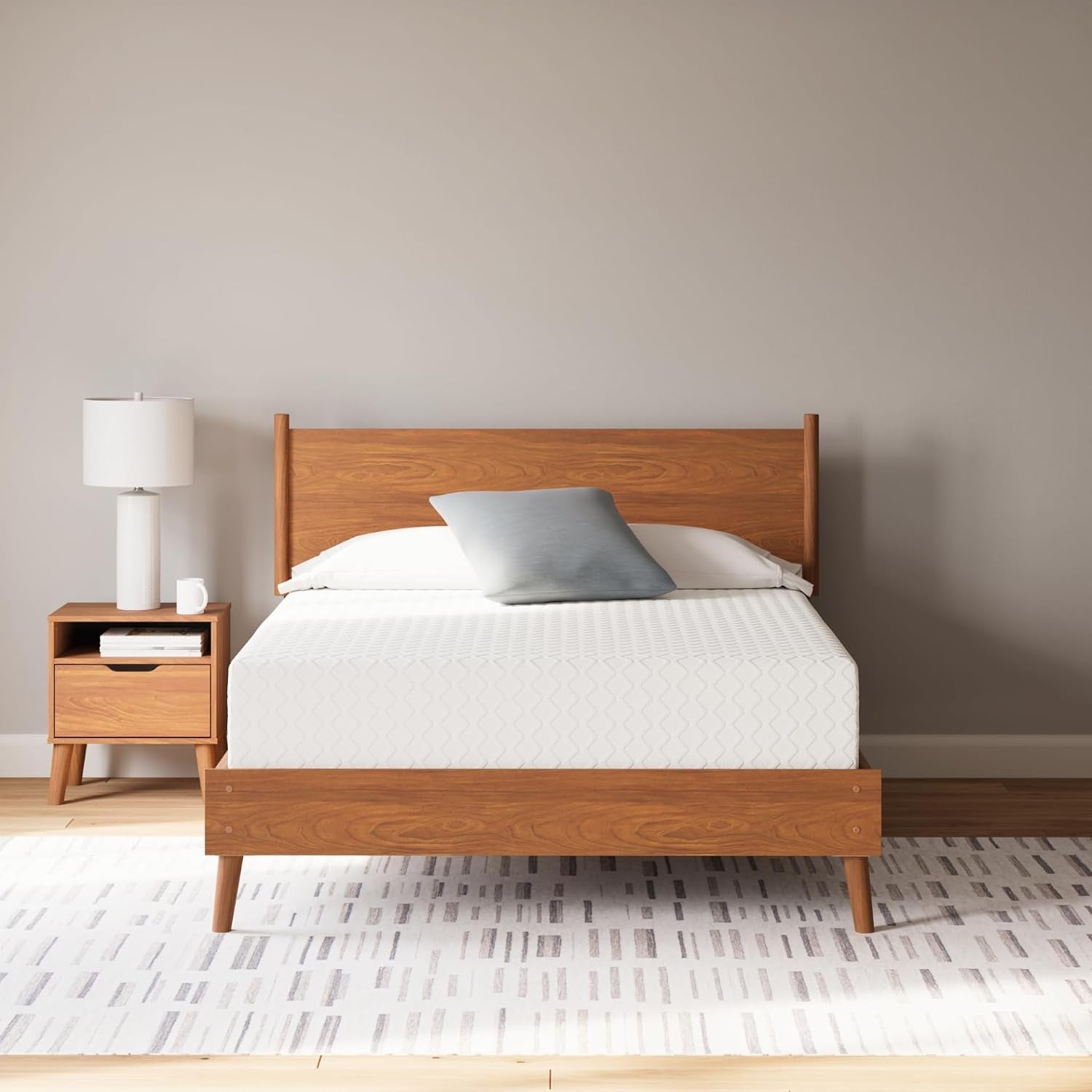 White mattress on a mid-century wooden bed frame in a neutral bedroom, front view with nightstand and lamp