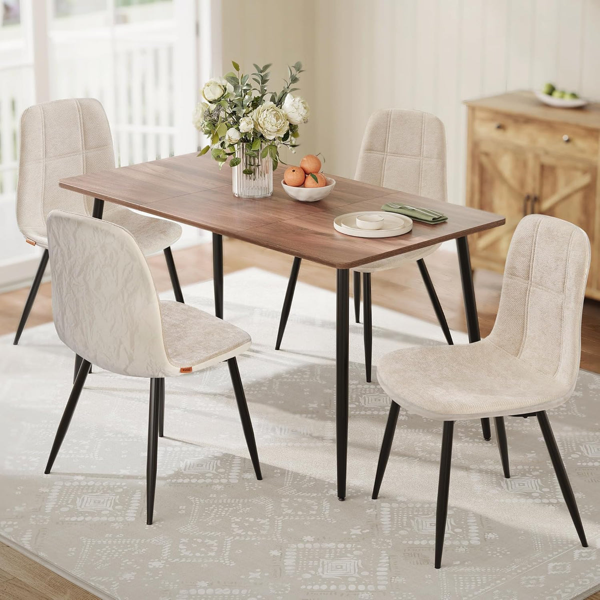 Cream white dining chairs with black metal legs around a wood dining table in a bright dining room