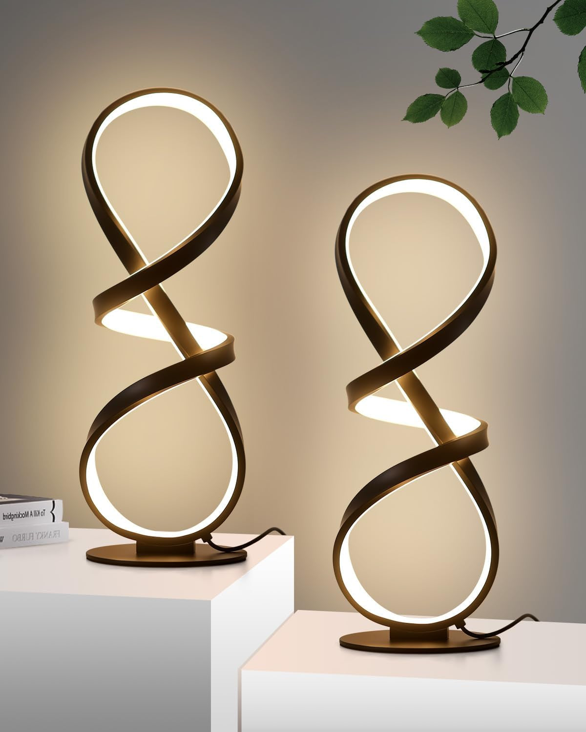 Two lit gold spiral lamps shown on stepped white pedestals against a warm background with a leafy branch above.