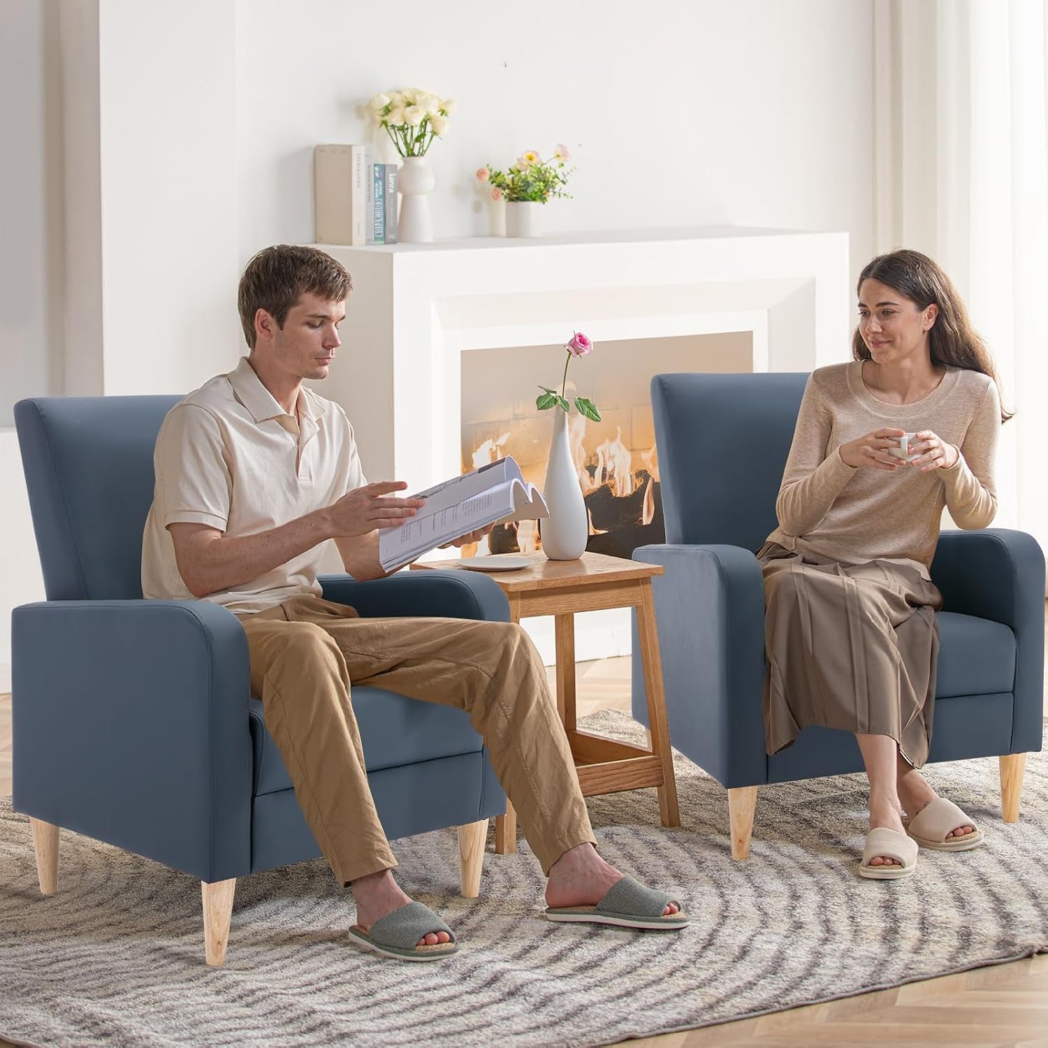 Two blue high-back chairs with wooden legs facing each other in a living room with a man and woman seated.