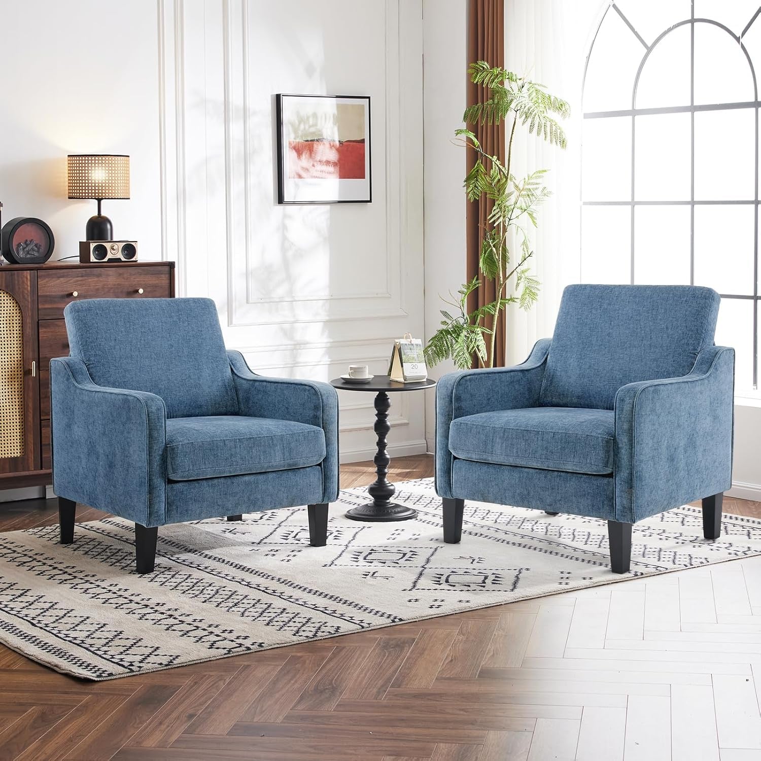 Two blue upholstered accent chairs flanking a small round black side table in a bright living space