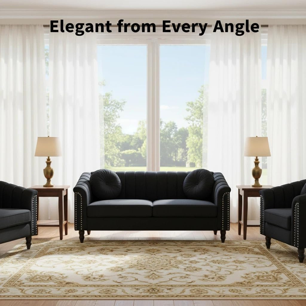 Front view of black velvet sofa with round bolster pillows centered before tall windows, chairs at edges.