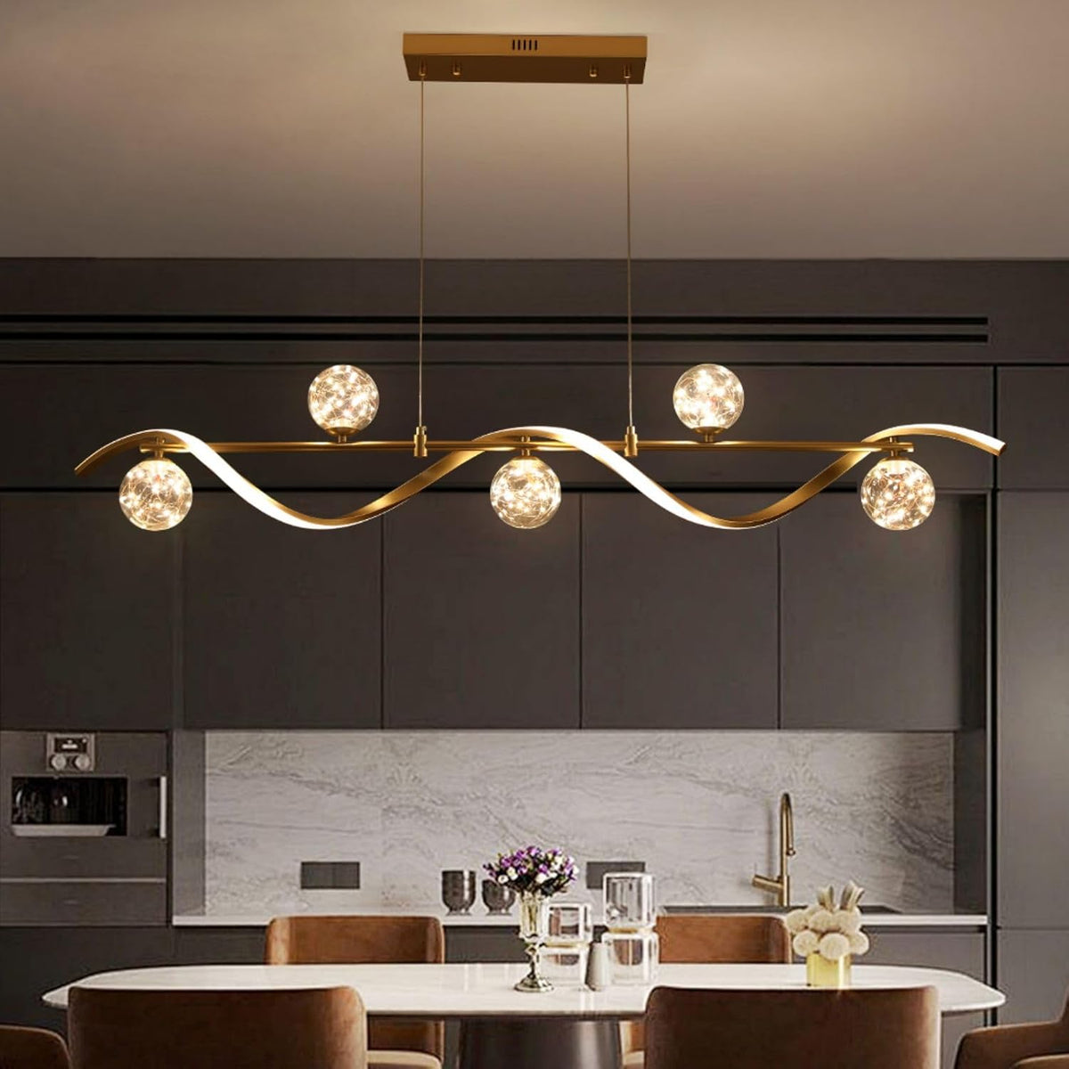 Gold linear chandelier with six illuminated clear glass globe shades over a dining table, frontal view