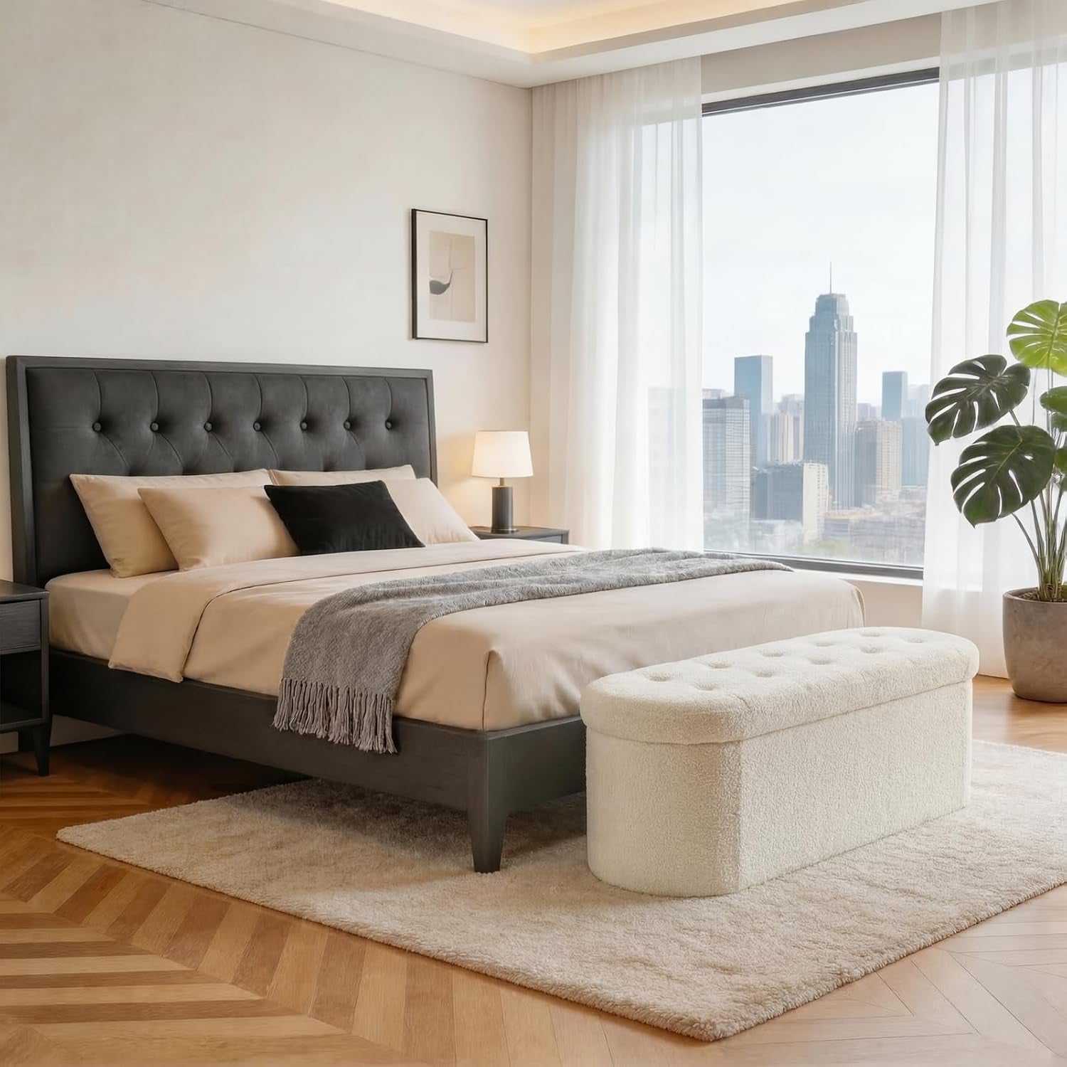 White tufted oval storage bench at foot of a bed in a bright, modern bedroom