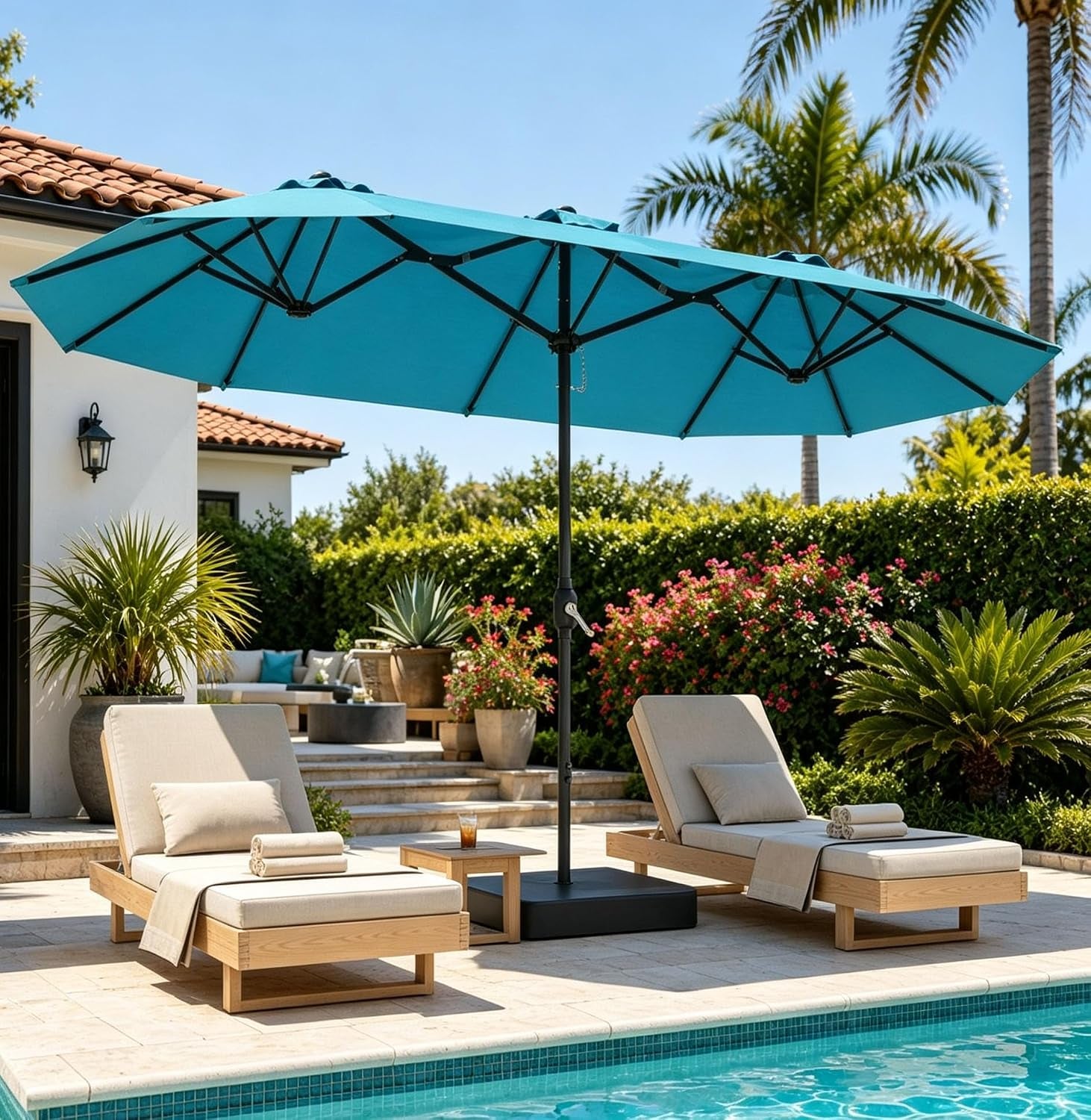 Outdoor pool deck with a teal umbrella shading two beige cushioned lounge chairs.