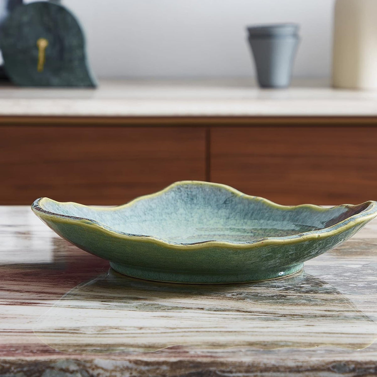 Low side profile of a shallow green ceramic bowl showing wavy rim and low pedestal base on a marble surface