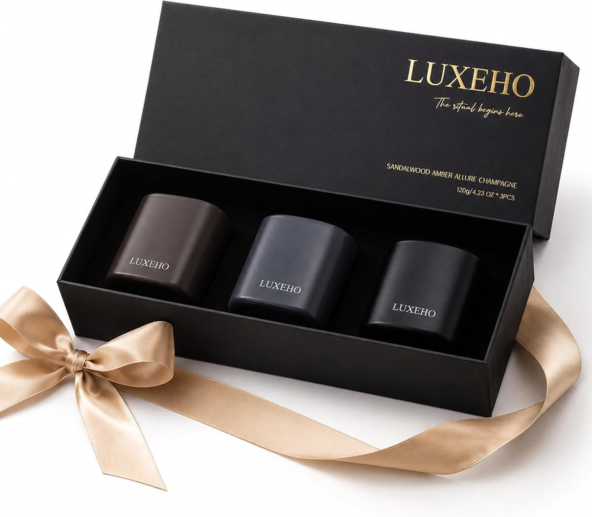 Open black gift box with three matte jars nestled inside shown beside a gold ribbon and bow on a white surface.