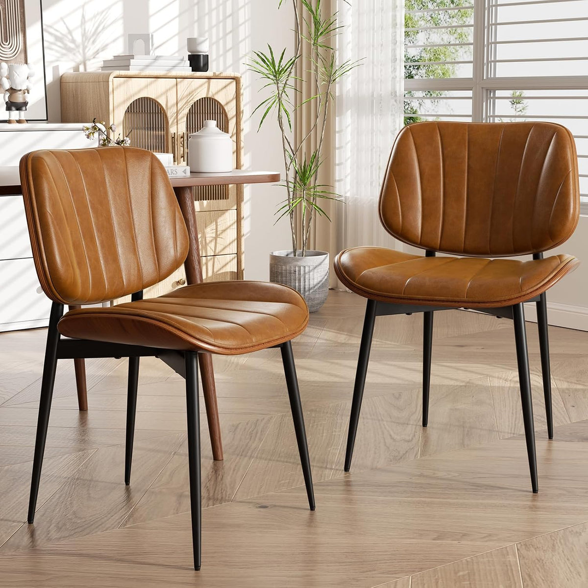 Two tan faux-leather dining chairs with stitched vertical channels and walnut backs shown in a bright room.