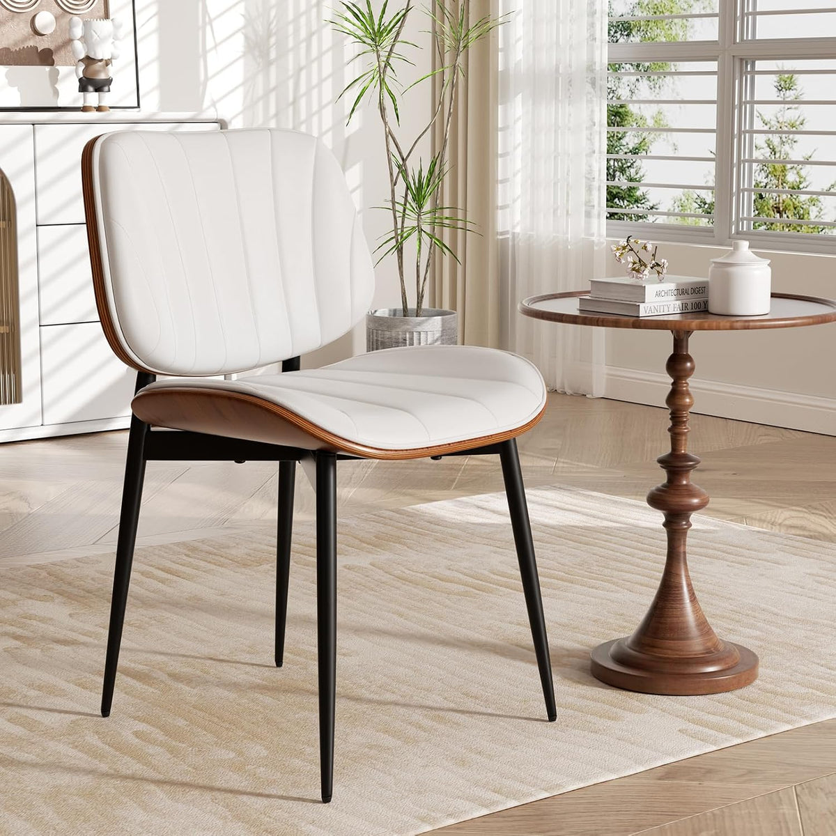 Close-up of a single white faux-leather dining chair with walnut edge and slim black metal legs next to a small round side