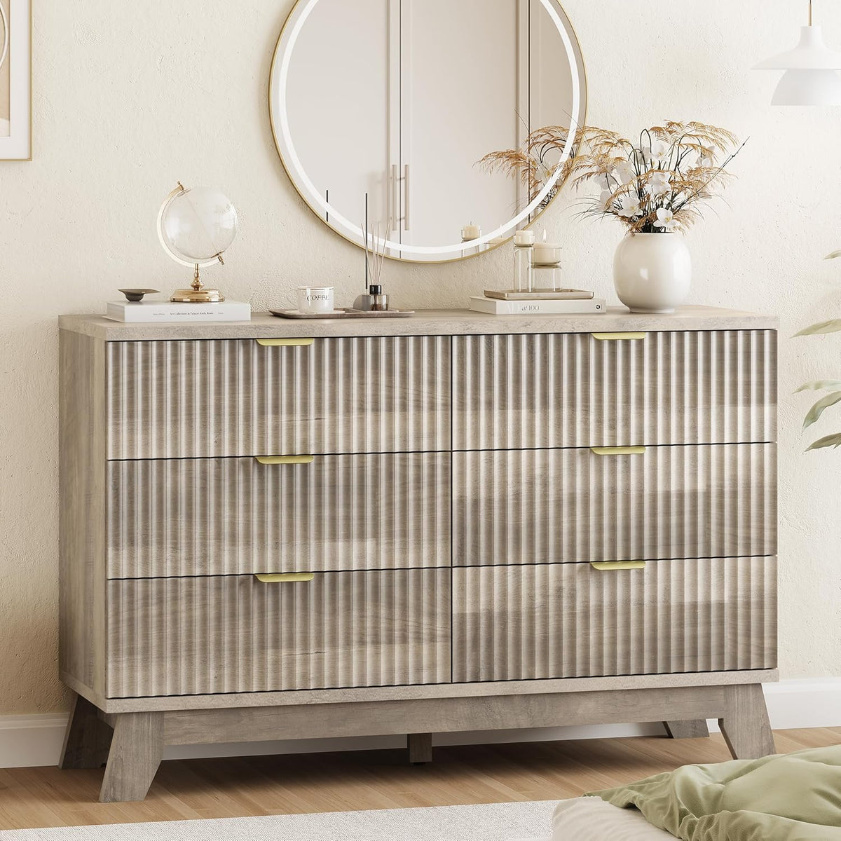 Close frontal view of a weathered gray wave-front dresser with gold handles and decorative vase