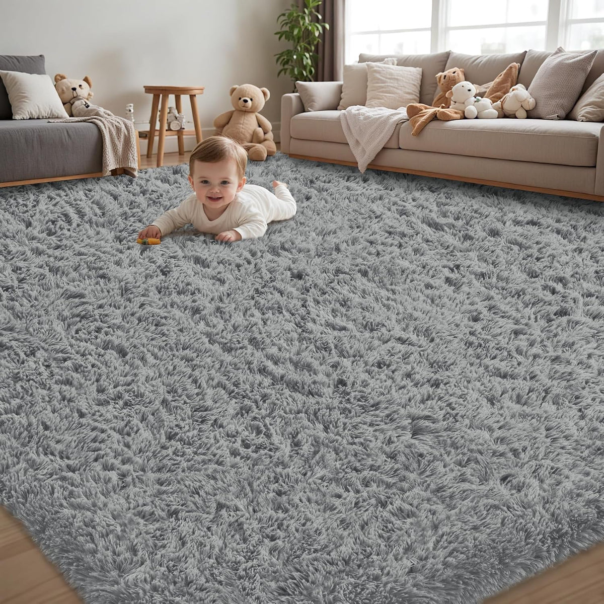 Infant on a plush gray shag rug in a living room with neutral sofas and a teddy bear.