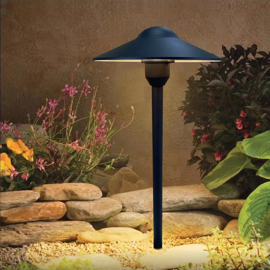 Close-up angled view of a black pathway light over decorative rocks and garden plants with warm glow