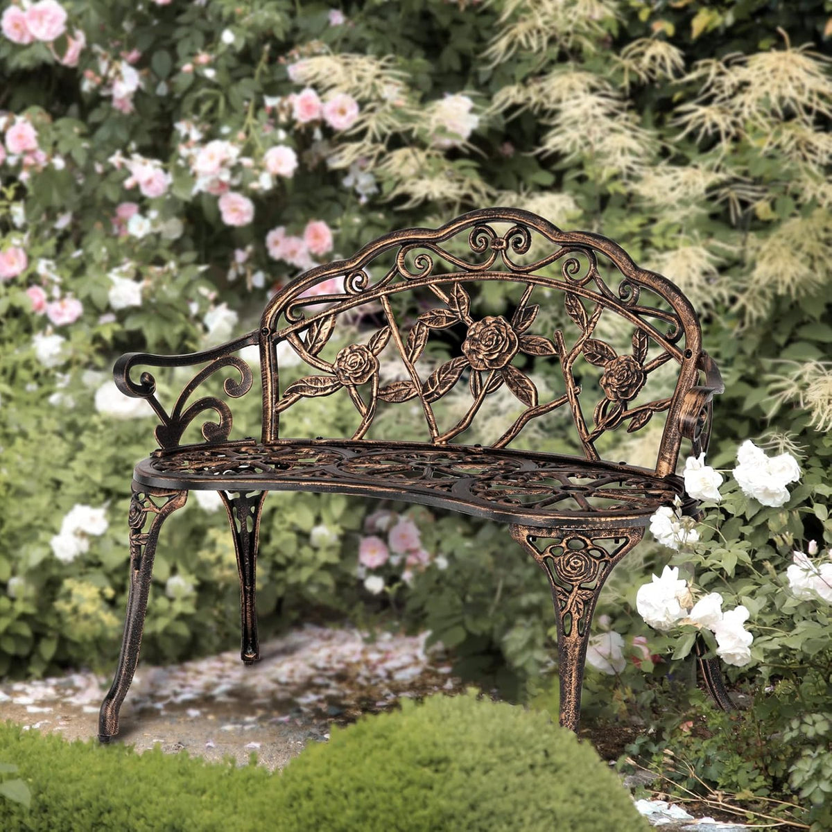 Curved two-person metal bench with rose motif placed in a lush garden among pink and white flowers