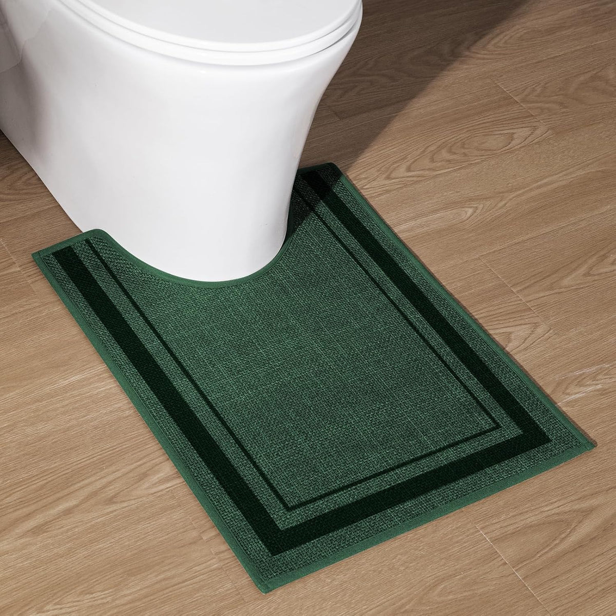U-shaped green contour rug fitted around base of a white toilet on wood flooring.