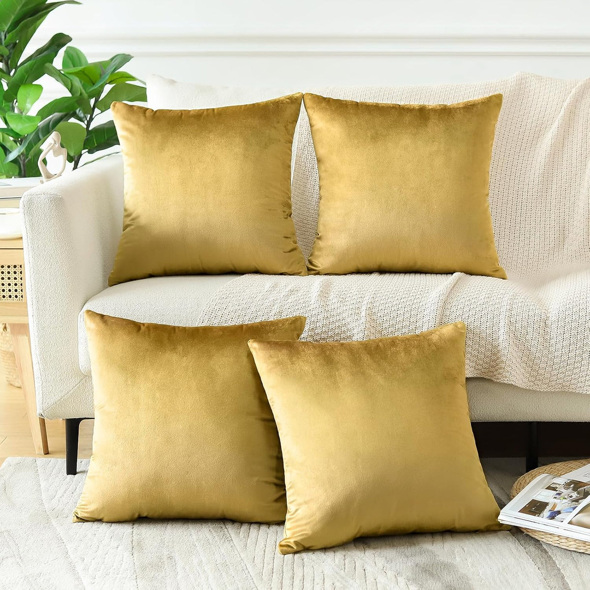 Four golden yellow square velvet pillow covers displayed on a cream couch and floor.
