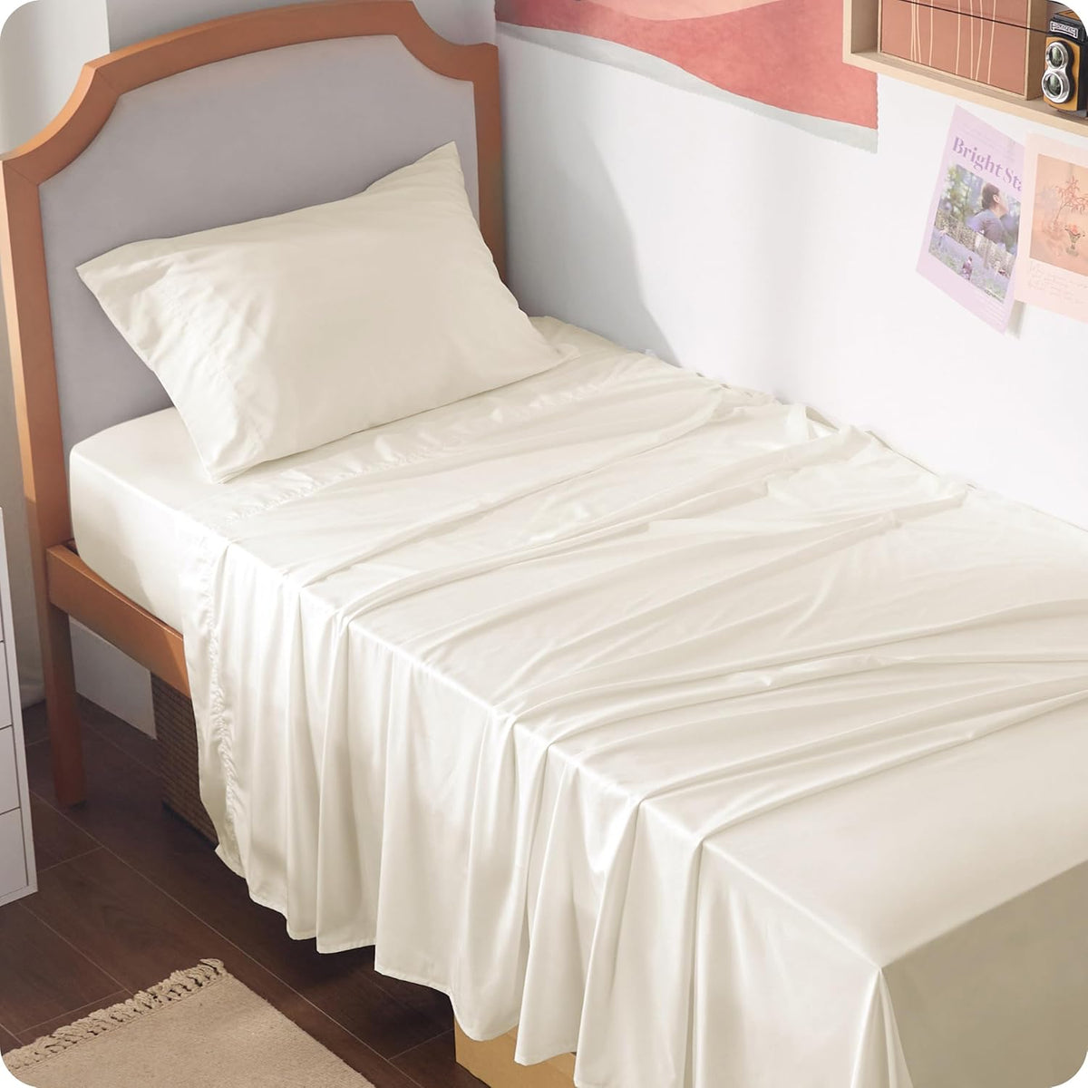 Cream/ivory sheets on a single bed with a light-upholstered headboard and small wall decor nearby.
