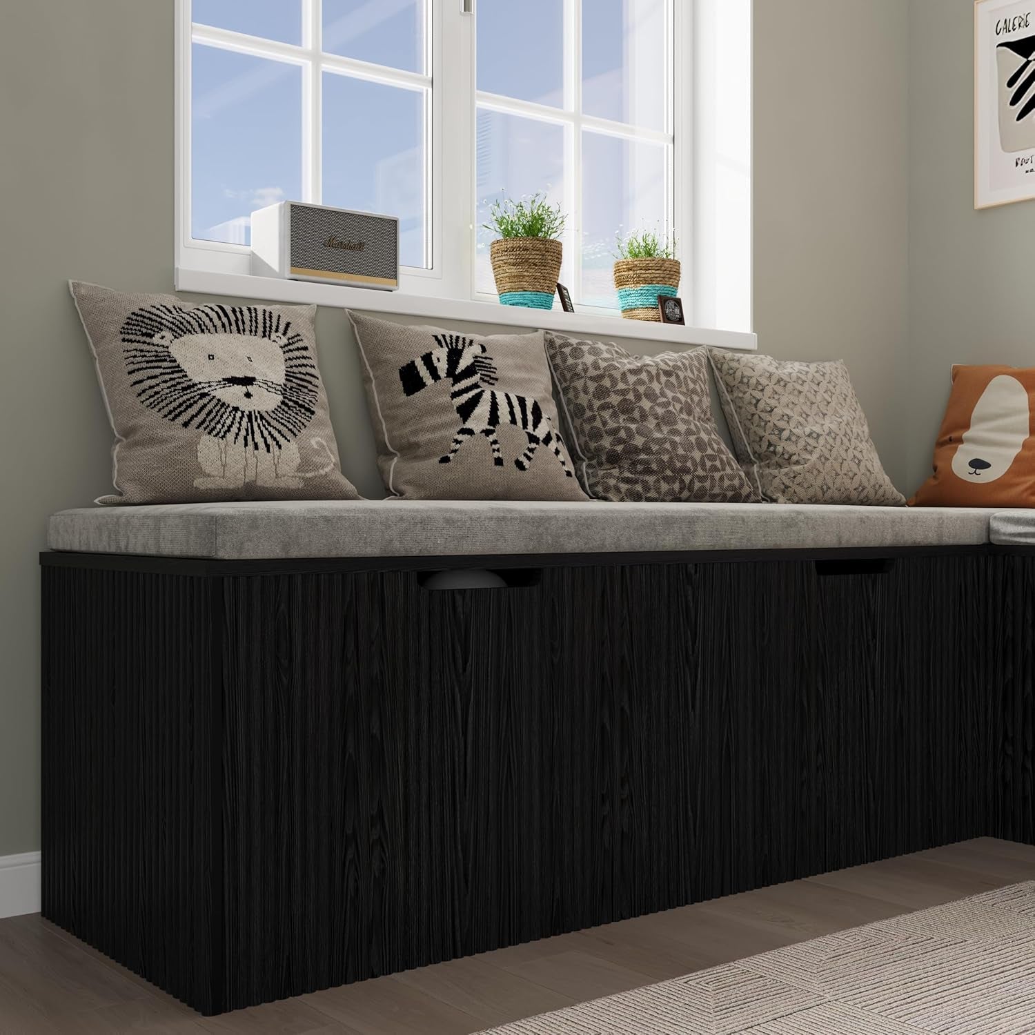 Side view of the black bench with light grey cushion and animal-print throw pillows beneath a window