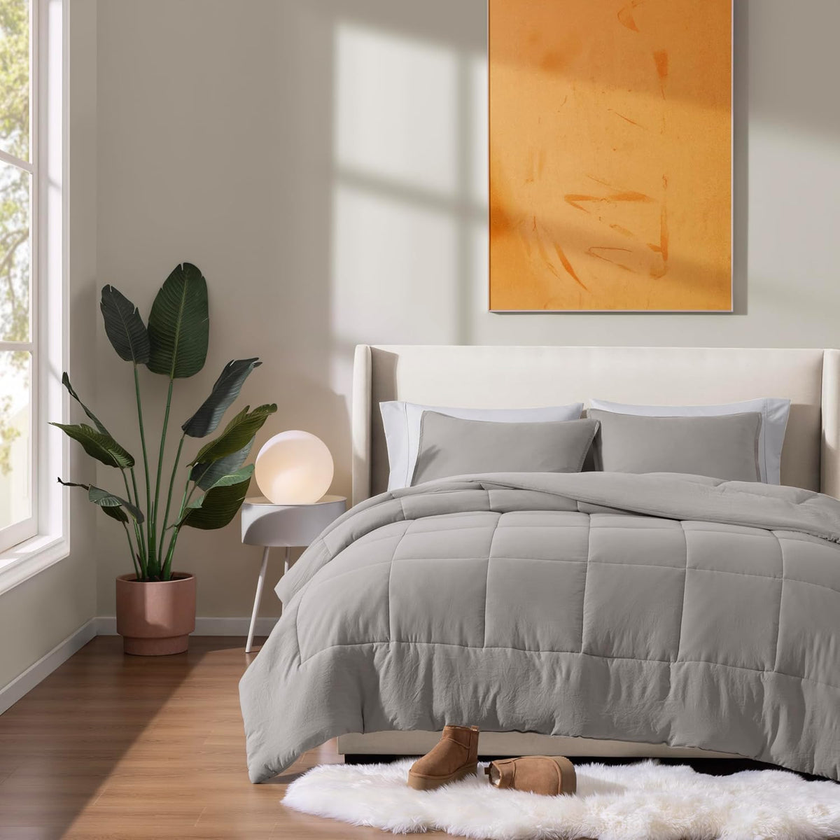 Styled bedroom with light grey comforter and shams, potted plant and framed art visible, front view