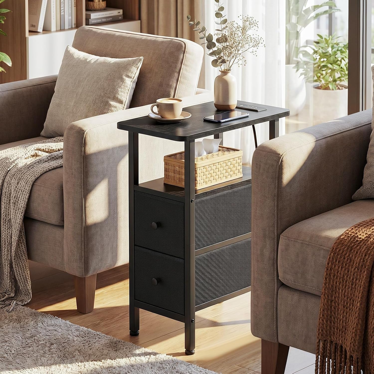 Black narrow side table positioned between two beige armchairs with a phone, mug and planter on the tabletop