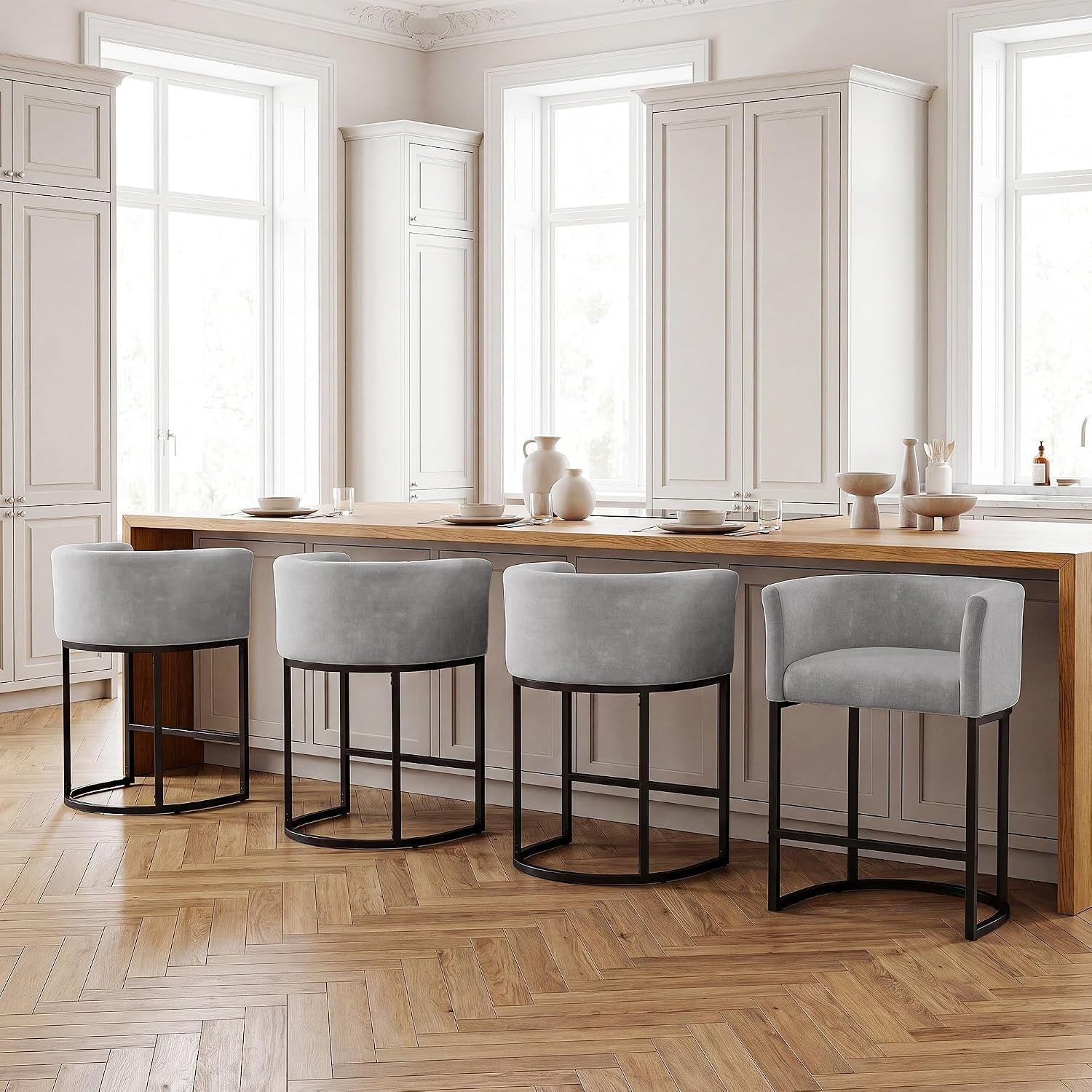 Four light-gray barrel-back counter stools lined along a wooden breakfast bar in a bright kitchen.
