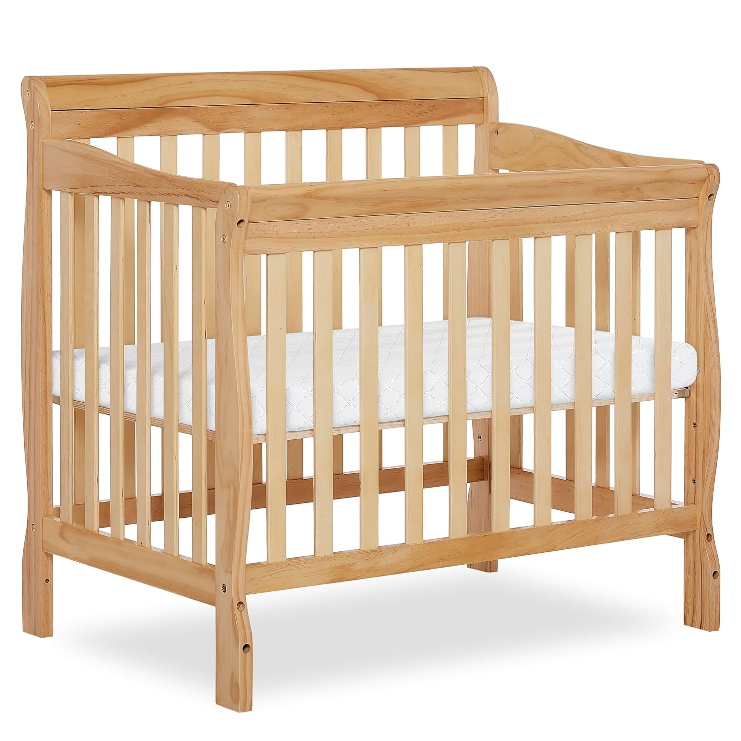 Light natural wood mini crib with curved headboard and slatted sides, shown with a white mattress
