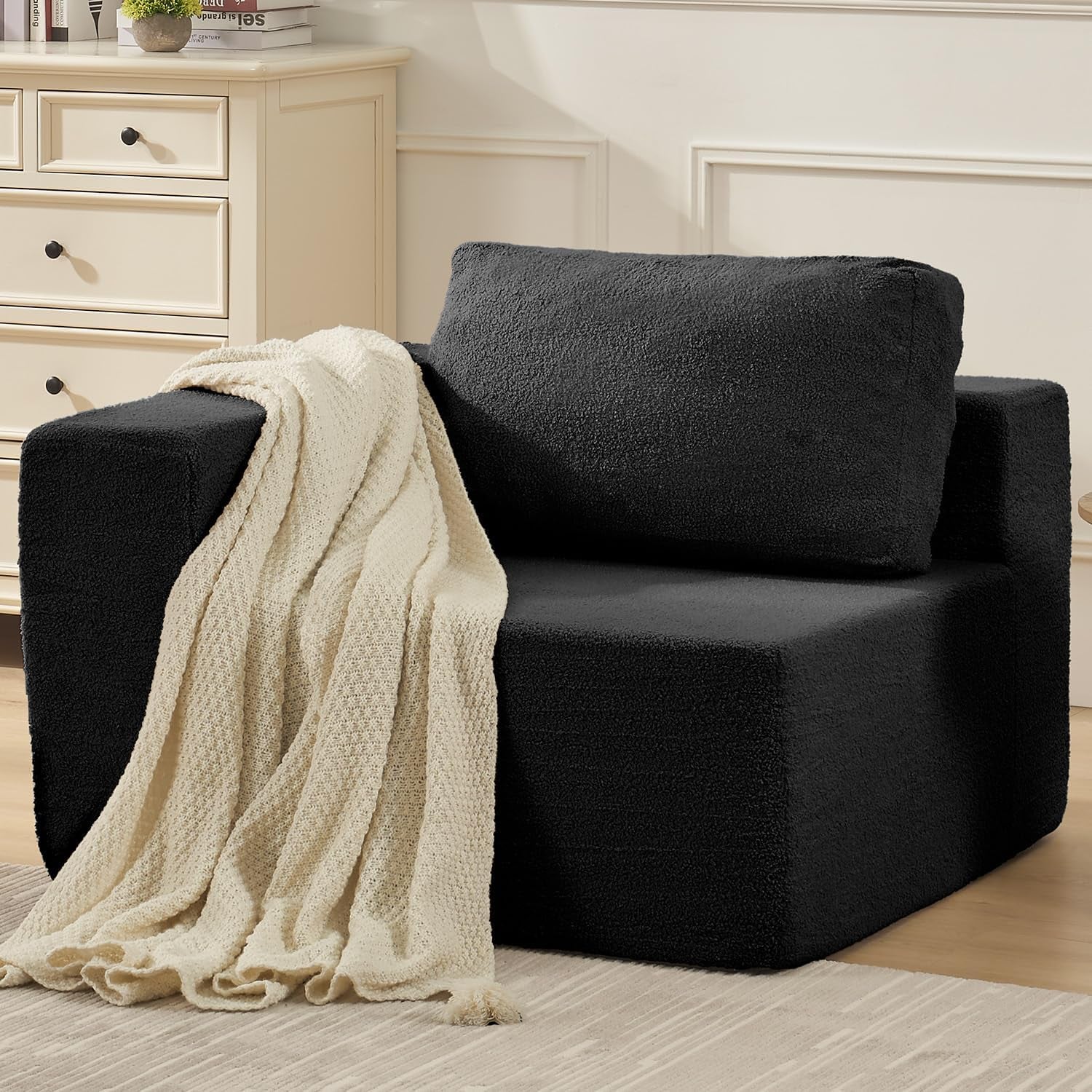 Close-up of a single black modular seat with a cream knit throw draped over the arm.