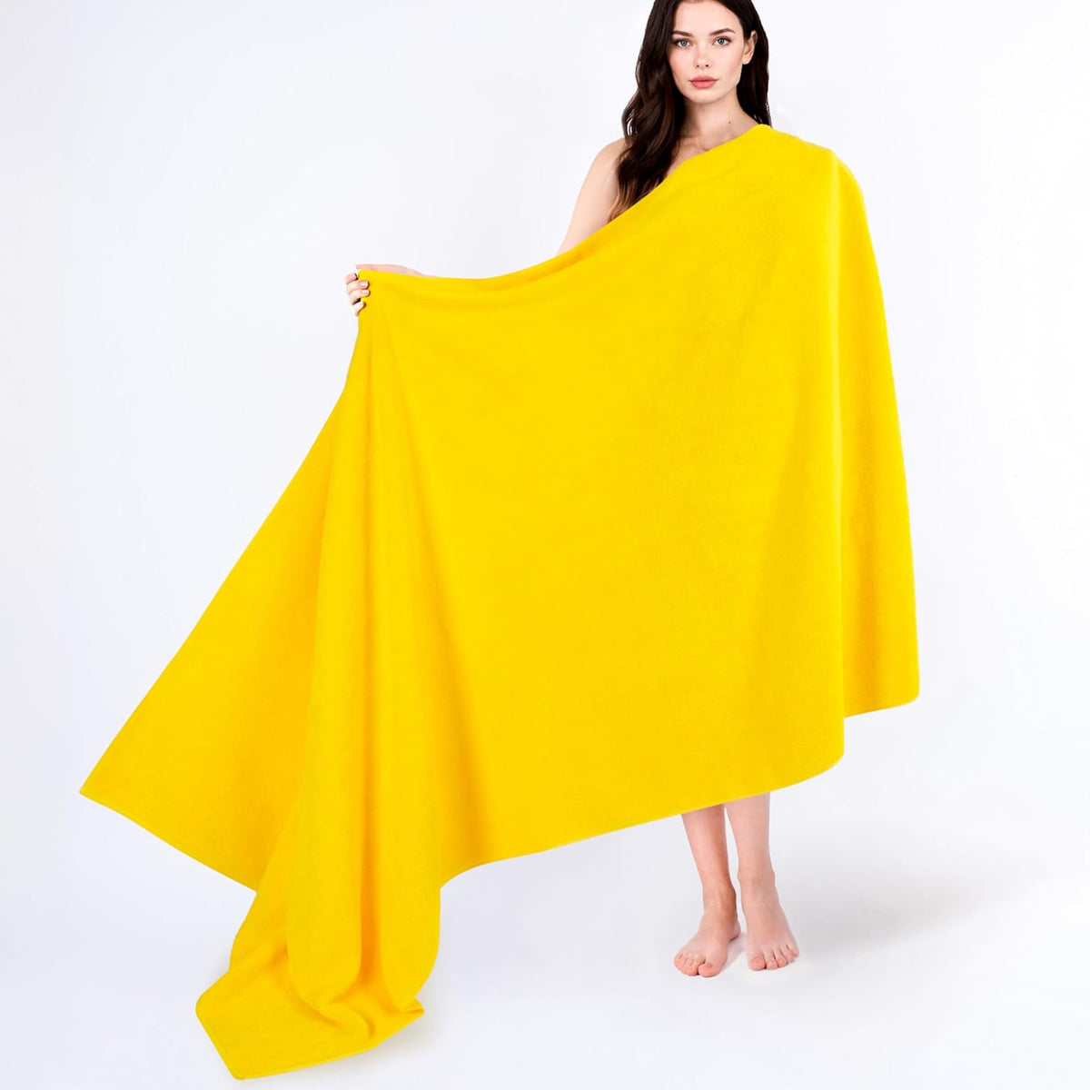 Full-length model standing barefoot holding a wide yellow towel spread out to show its full drape and coverage.