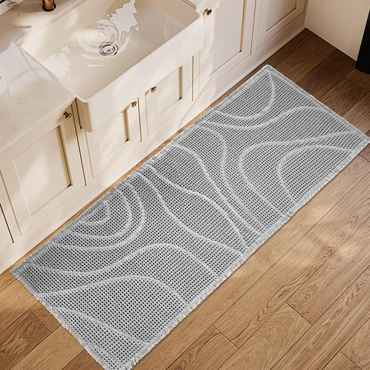 Light gray rectangular mat with wavy raised pattern placed in front of a sink on wood floor.