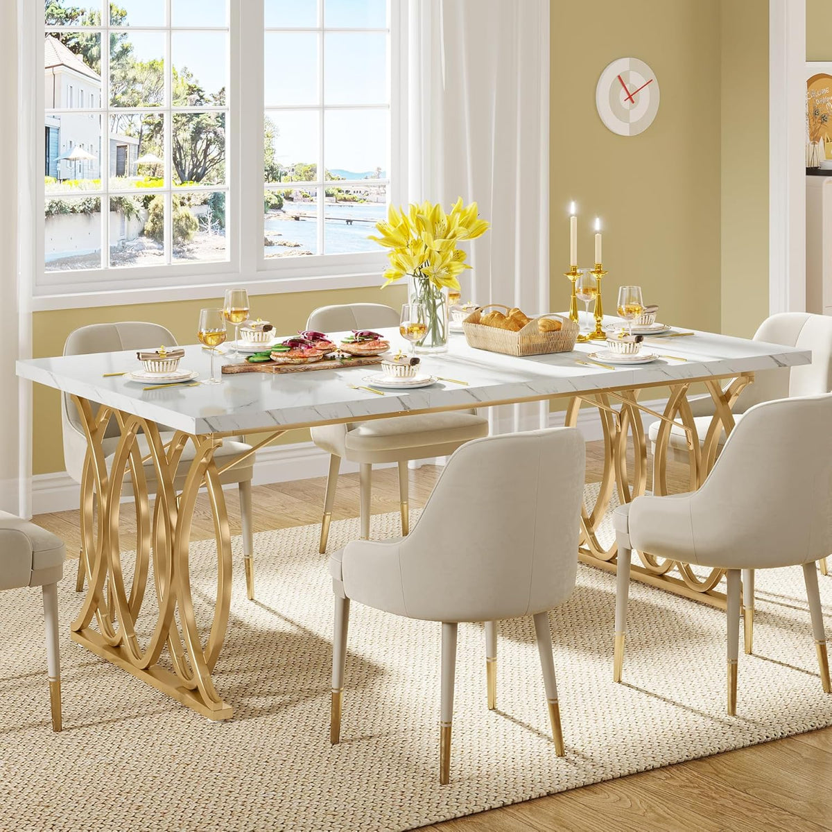 White faux marble dining table with gold geometric legs in a bright dining room surrounded by cream upholstered chairs