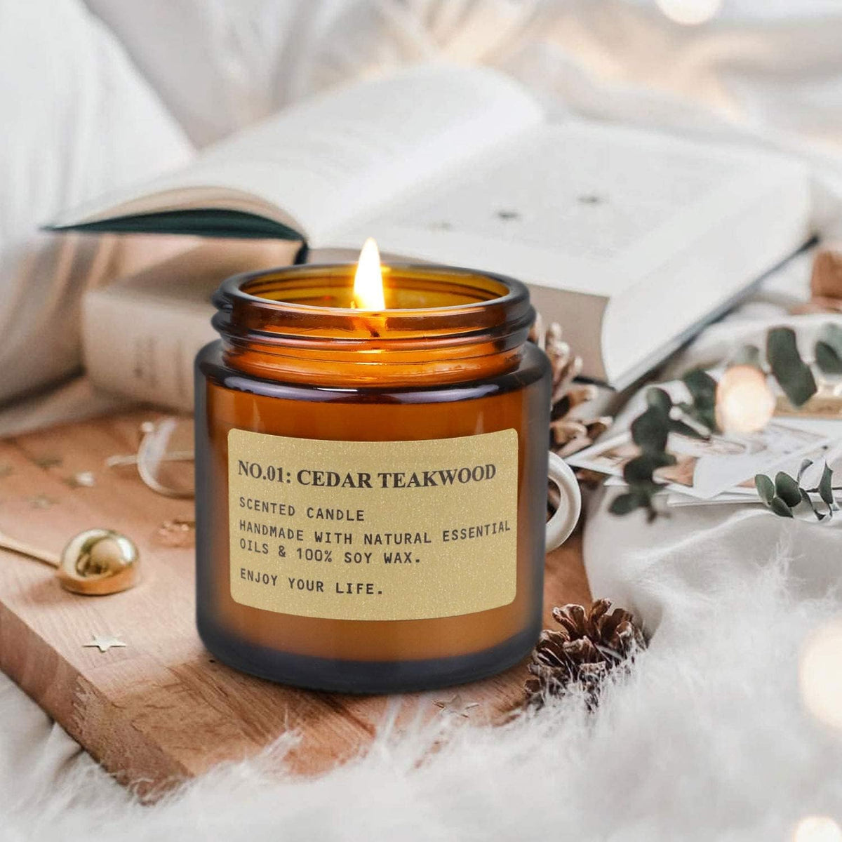 Lit amber jar candle on a bedside table with an open book and soft pillows in the background