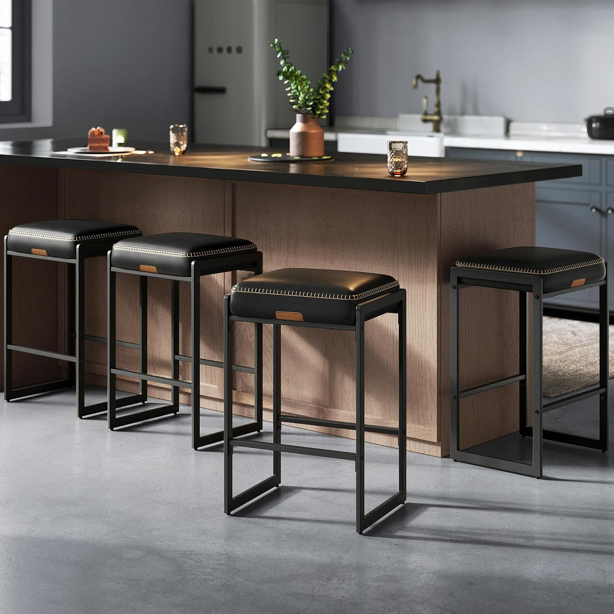 Four black-cushioned counter stools lined up along a kitchen island with a dark countertop and decorative vase on top.